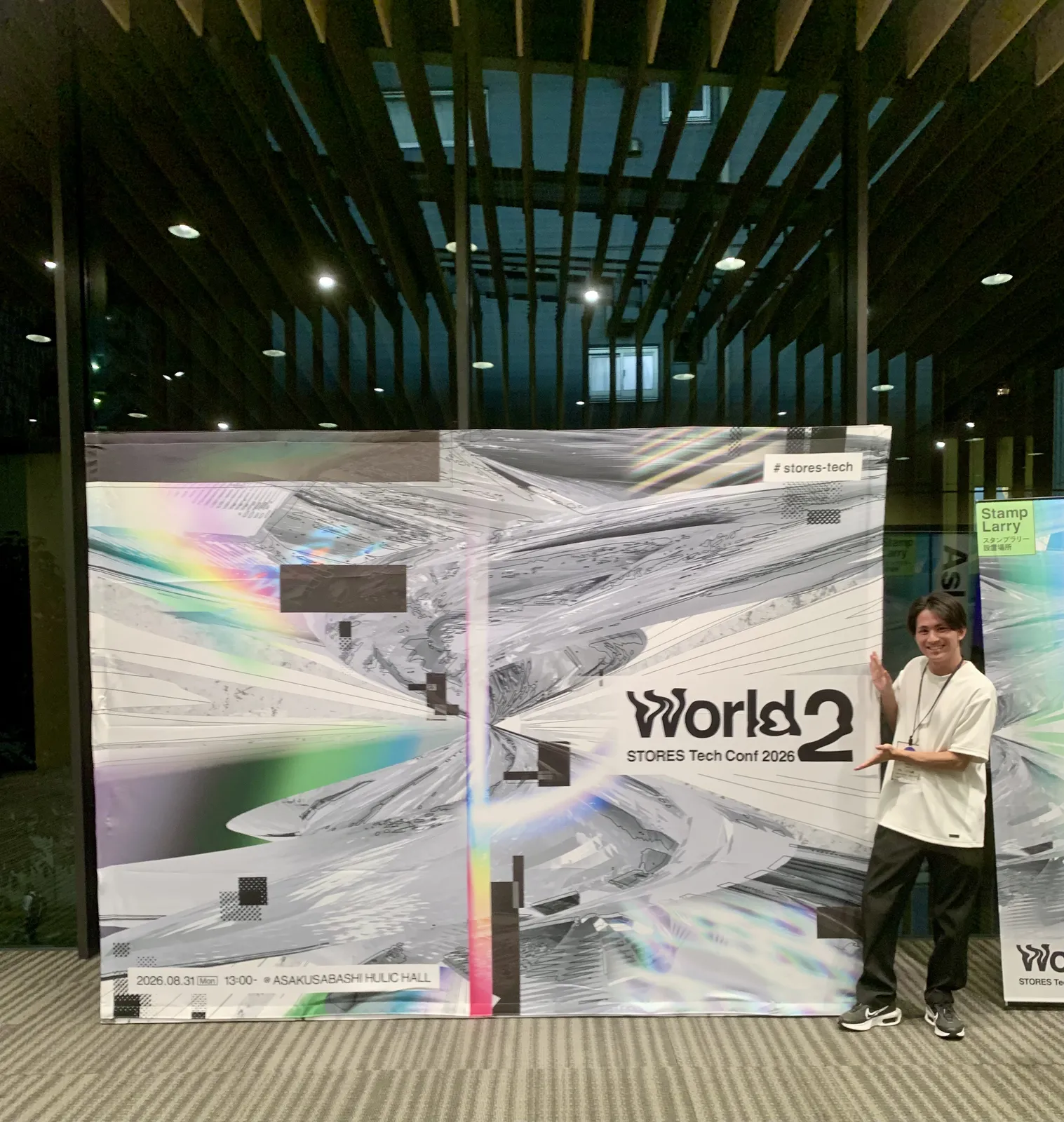 会場入口の「World 2 / STORES Tech Conf 2026」フォトウォールの前に立つ筆者